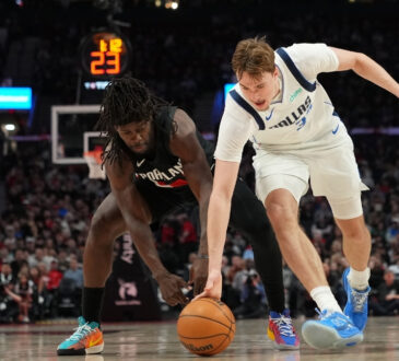 Cooper Flagg #32 of the Dallas Mavericks and Jrue Holiday #5 of the Portland Trail Blazers dive for a loose ball at Moda Center.