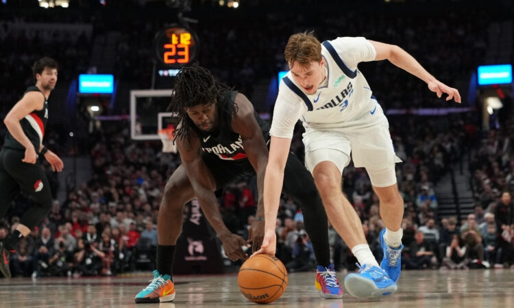 Cooper Flagg #32 of the Dallas Mavericks and Jrue Holiday #5 of the Portland Trail Blazers dive for a loose ball at Moda Center.