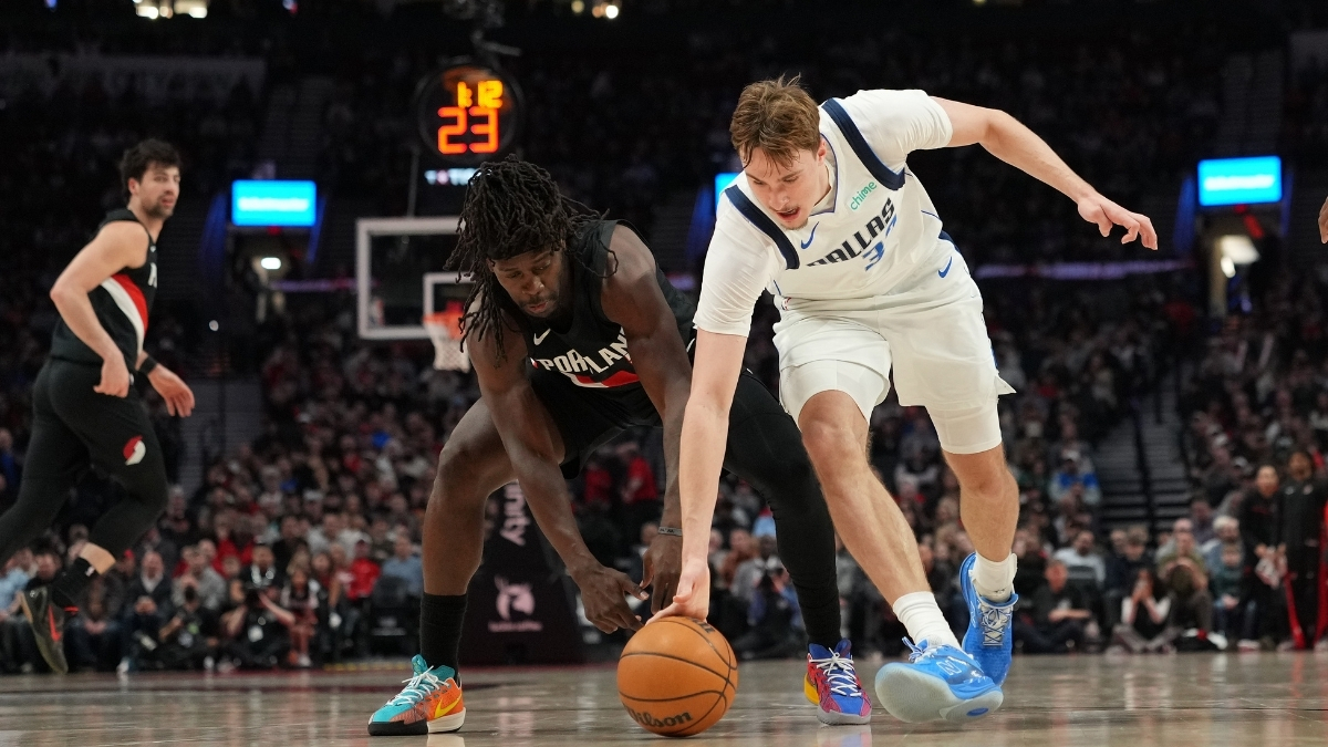 Cooper Flagg #32 of the Dallas Mavericks and Jrue Holiday #5 of the Portland Trail Blazers dive for a loose ball at Moda Center.