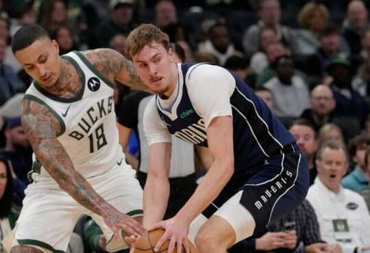 Cooper Flagg #32 of the Dallas Mavericks attempts a steal against Kyle Kuzma #18 of the Milwaukee Bucks during the first quarter at Fiserv Forum.