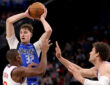 Cooper Flagg #32 of the Dallas Mavericks looks to pass while being guarded by Kris Dunn #8 and Brook Lopez #11 of the Los Angeles Clippers at Intuit Dome.