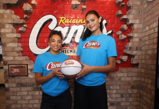 UCLA stars Lauren Betts and Kiki Rice posing with a basketball inside a Raising Cane’s restaurant in Hollywood after winning the 2026 NCAA Championship.