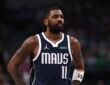 Guard Kyrie Irving wearing a white Dallas Mavericks jersey, looking on intently during a break in the action against the Denver Nuggets.