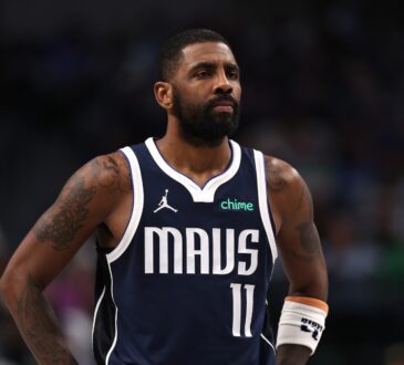 Guard Kyrie Irving wearing a white Dallas Mavericks jersey, looking on intently during a break in the action against the Denver Nuggets.