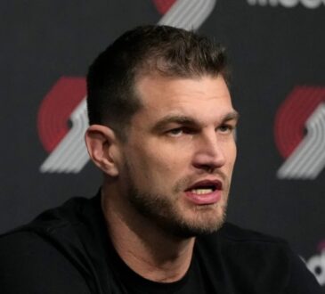 Tiago Splitter speaking at a Portland Trail Blazers press conference in front of a Moda and Trail Blazers logo backdrop