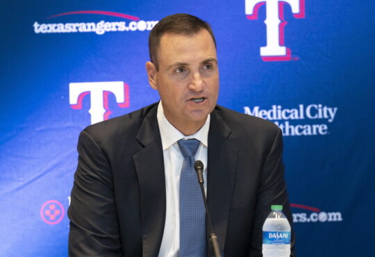 Texas Rangers general manager Chris Young speaks into a microphone in front of a Rangers backdrop at Globe Life Field.