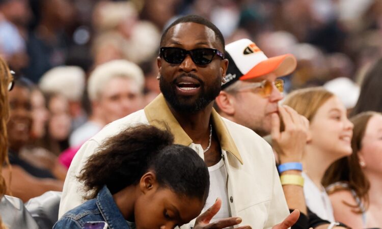 Dwyane Wade sits courtside in sunglasses and a cream jacket during the 2026 WNBA All-Star Game at United Center in Chicago.