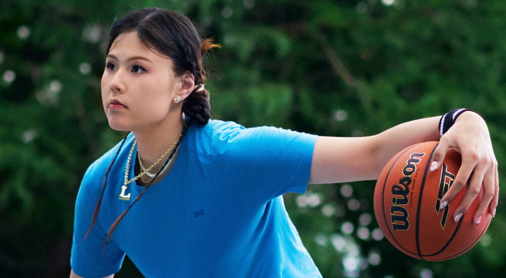 Dallas Wings center Li Yueru palms a Wilson basketball in Under Armour apparel on an outdoor court.