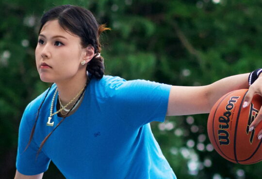 Dallas Wings center Li Yueru palms a Wilson basketball in Under Armour apparel on an outdoor court.