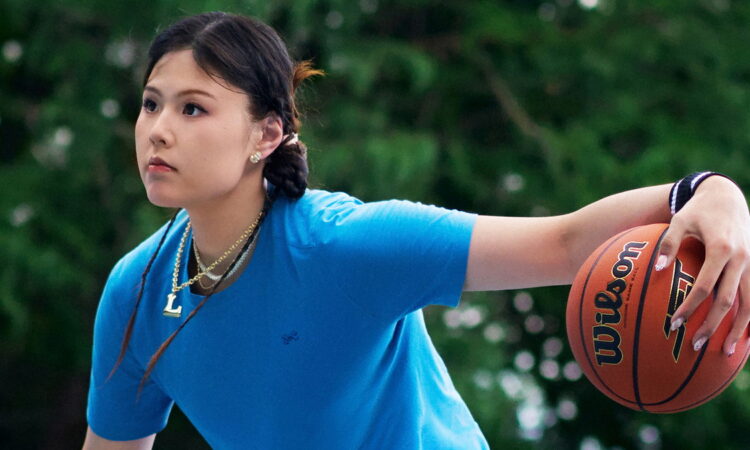 Dallas Wings center Li Yueru palms a Wilson basketball in Under Armour apparel on an outdoor court.