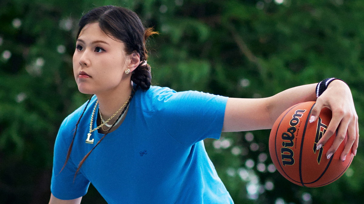 Dallas Wings center Li Yueru palms a Wilson basketball in Under Armour apparel on an outdoor court.