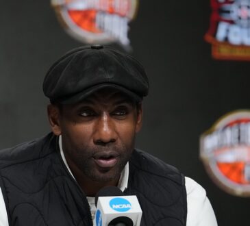 Amar'e Stoudemire speaks into an NCAA microphone at the Naismith Hall of Fame press conference in a flat cap and black vest.