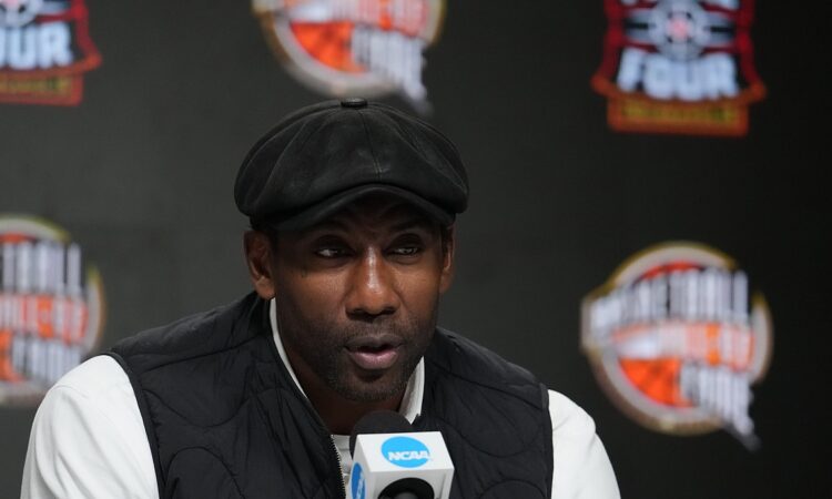 Amar'e Stoudemire speaks into an NCAA microphone at the Naismith Hall of Fame press conference in a flat cap and black vest.