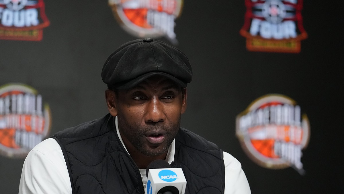 Amar'e Stoudemire speaks into an NCAA microphone at the Naismith Hall of Fame press conference in a flat cap and black vest.