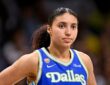 Dallas Wings guard Azzi Fudd stands with a hand on her hip in a blue Dallas jersey, looking toward the court.