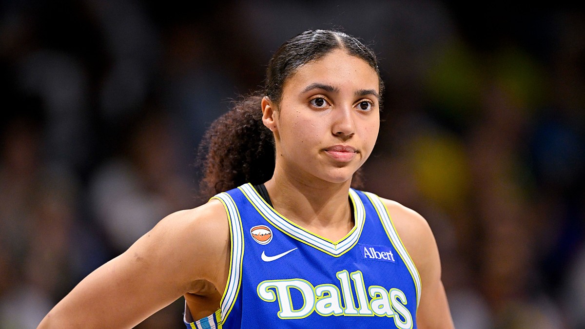 Dallas Wings guard Azzi Fudd stands with a hand on her hip in a blue Dallas jersey, looking toward the court.