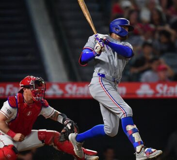 Texas Rangers right fielder Brandon Nimmo follows through on a swing as the Angels catcher watches from his knees.