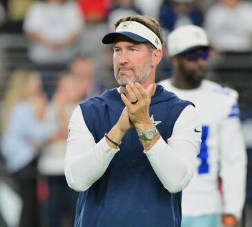 Dallas Cowboys head coach Brian Schottenheimer claps as he watches pregame warmups on the field.