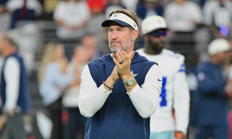 Dallas Cowboys head coach Brian Schottenheimer claps as he watches pregame warmups on the field.