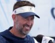 Dallas Cowboys head coach Brian Schottenheimer smiles while speaking at a microphone during a press conference.