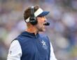 Dallas Cowboys head coach Brian Schottenheimer calls out from the sideline wearing a headset.