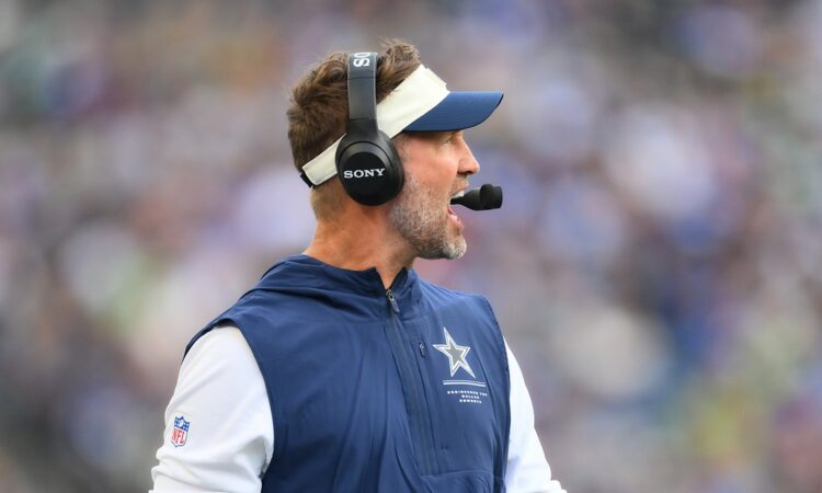 Dallas Cowboys head coach Brian Schottenheimer calls out from the sideline wearing a headset.