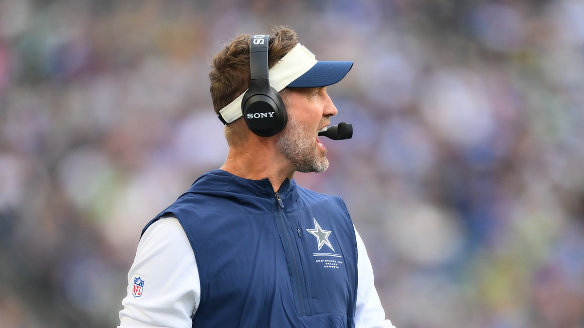Dallas Cowboys head coach Brian Schottenheimer calls out from the sideline wearing a headset.