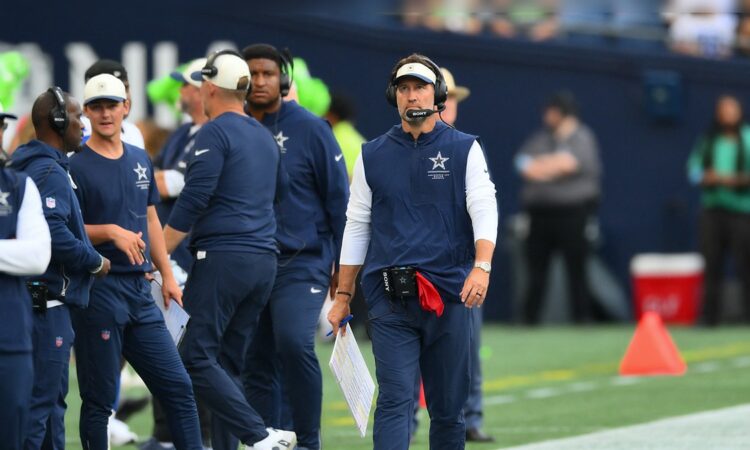 Dallas Cowboys head coach Brian Schottenheimer walks the sideline in a headset, holding a play sheet.