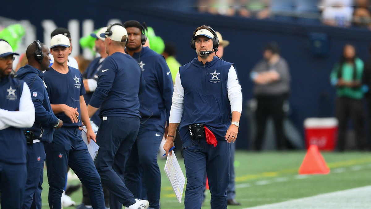 Dallas Cowboys head coach Brian Schottenheimer walks the sideline in a headset, holding a play sheet.