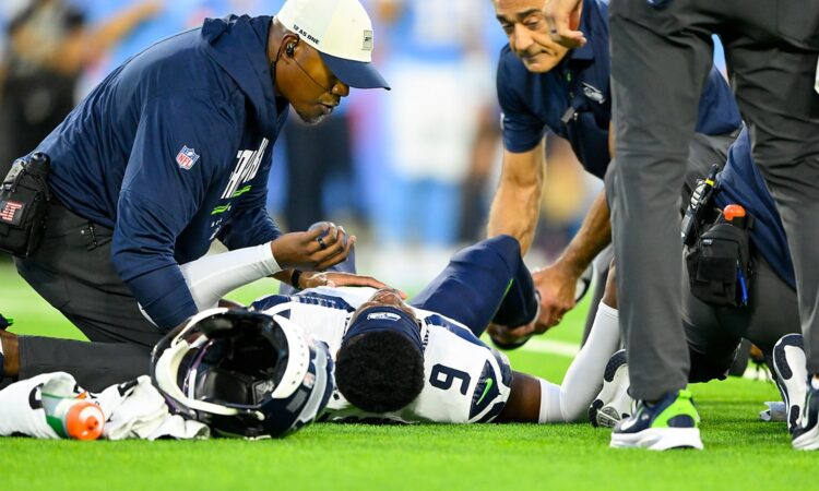 Seattle Seahawks trainers kneel over safety Bud Clark on the field after a leg injury.