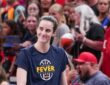 Indiana Fever guard Caitlin Clark smiles as she walks onto the court in a Fever warmup shirt before tipoff.