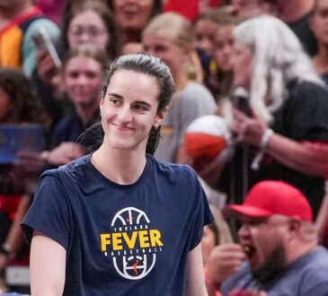 Indiana Fever guard Caitlin Clark smiles as she walks onto the court in a Fever warmup shirt before tipoff.