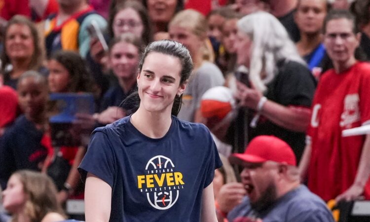 Indiana Fever guard Caitlin Clark smiles as she walks onto the court in a Fever warmup shirt before tipoff.