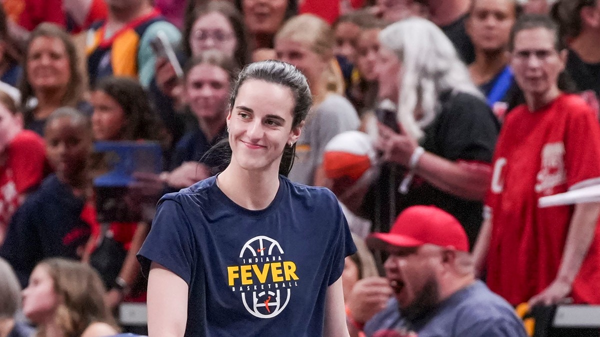 Indiana Fever guard Caitlin Clark smiles as she walks onto the court in a Fever warmup shirt before tipoff.