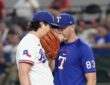 Texas Rangers pitching coach Jordan Tiegs talks with pitcher Cal Quantrill on the mound, both covering their mouths.