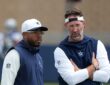 Dallas Cowboys defensive coordinator Christian Parker stands beside head coach Brian Schottenheimer, who talks with his arms folded, during training camp.