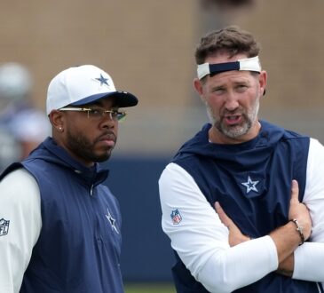 Dallas Cowboys defensive coordinator Christian Parker stands beside head coach Brian Schottenheimer, who talks with his arms folded, during training camp.