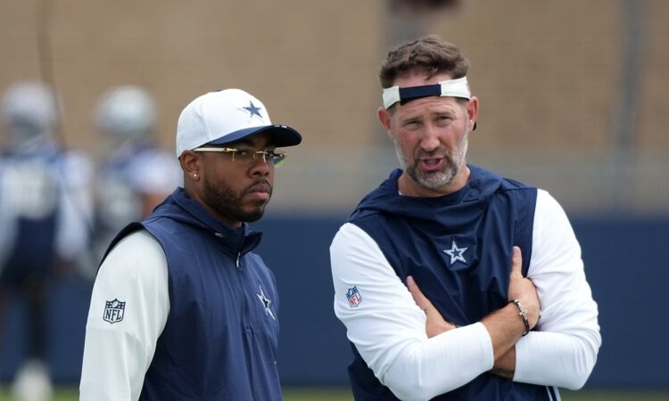 Dallas Cowboys defensive coordinator Christian Parker stands beside head coach Brian Schottenheimer, who talks with his arms folded, during training camp.
