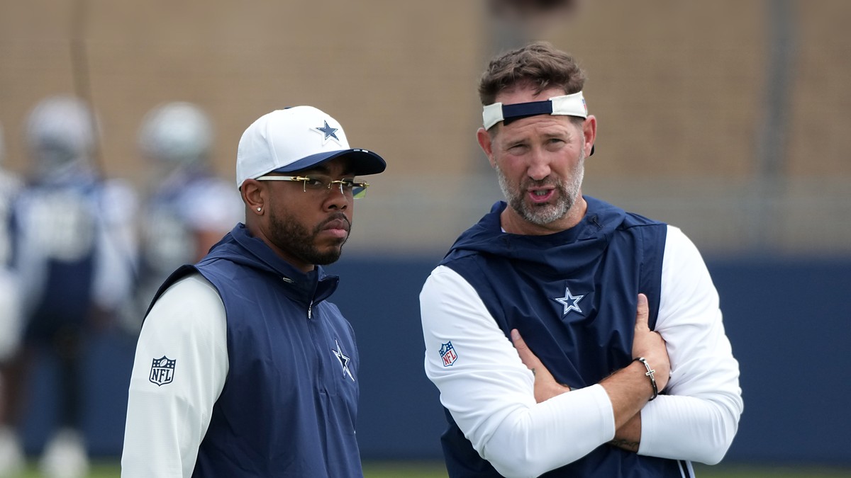 Dallas Cowboys defensive coordinator Christian Parker stands beside head coach Brian Schottenheimer, who talks with his arms folded, during training camp.