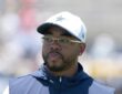 Dallas Cowboys defensive coordinator Christian Parker watches practice in a white Cowboys cap and navy vest.