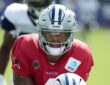 Dallas Cowboys quarterback Dak Prescott leans under center in a red non-contact jersey during joint practice.