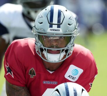 Dallas Cowboys quarterback Dak Prescott leans under center in a red non-contact jersey during joint practice.