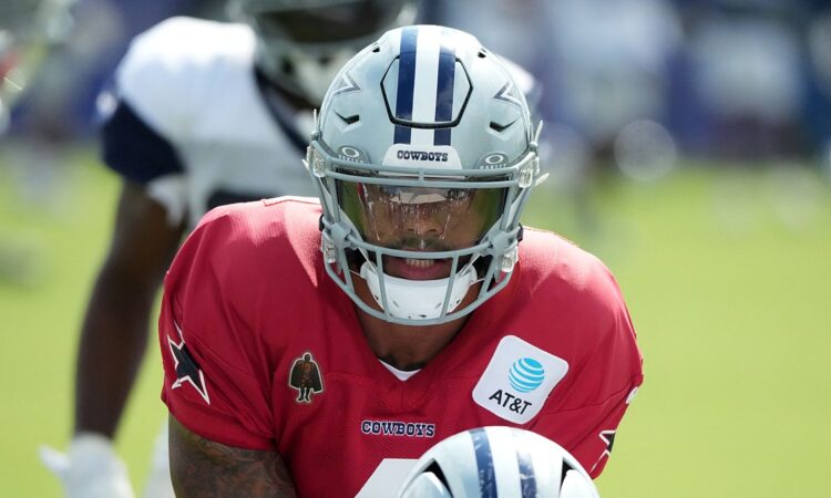 Dallas Cowboys quarterback Dak Prescott leans under center in a red non-contact jersey during joint practice.