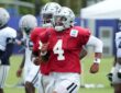 Dallas Cowboys quarterback Dak Prescott runs upfield in a red non-contact jersey, grinning behind his facemask.
