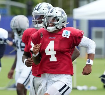 Dallas Cowboys quarterback Dak Prescott runs upfield in a red non-contact jersey, grinning behind his facemask.