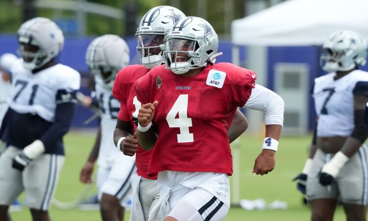 Dallas Cowboys quarterback Dak Prescott runs upfield in a red non-contact jersey, grinning behind his facemask.