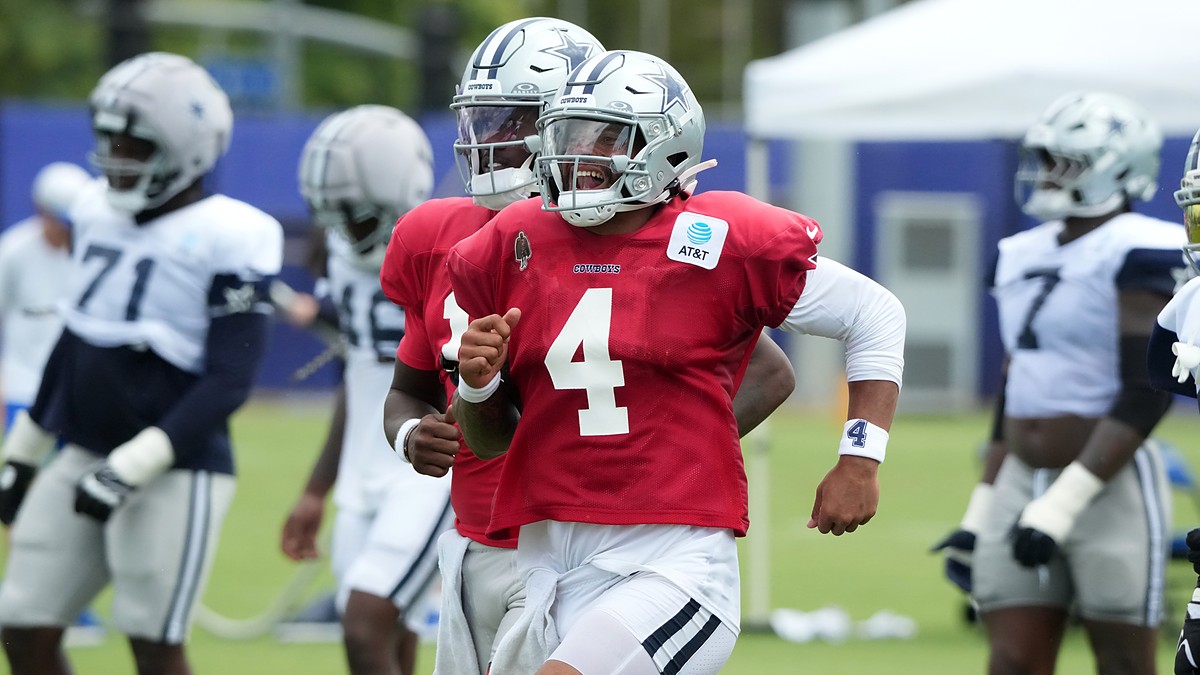 Dallas Cowboys quarterback Dak Prescott runs upfield in a red non-contact jersey, grinning behind his facemask.