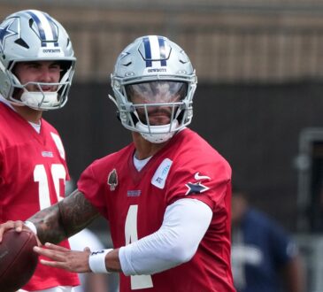 Dallas Cowboys quarterback Dak Prescott holds the football during a drill as quarterback Sam Howell looks on.