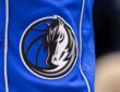Close view of the Dallas Mavericks horse-head logo stitched on the leg of blue team shorts.