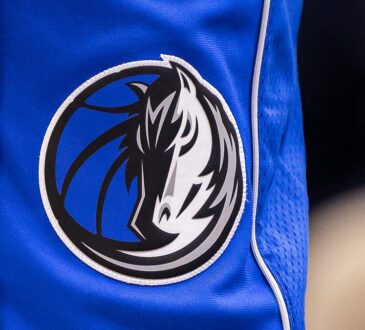 Close view of the Dallas Mavericks horse-head logo stitched on the leg of blue team shorts.